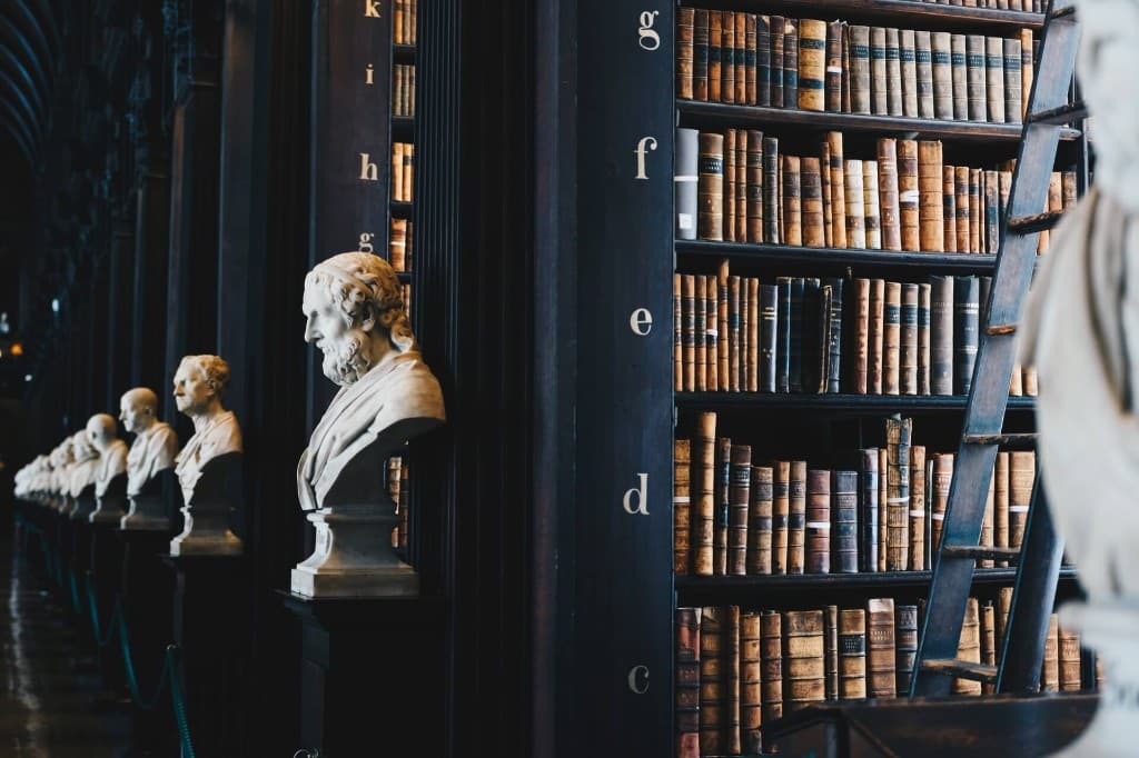 Rangée de bustes en marbre dans une bibliothèque historique aux rayonnages remplis de livres anciens.